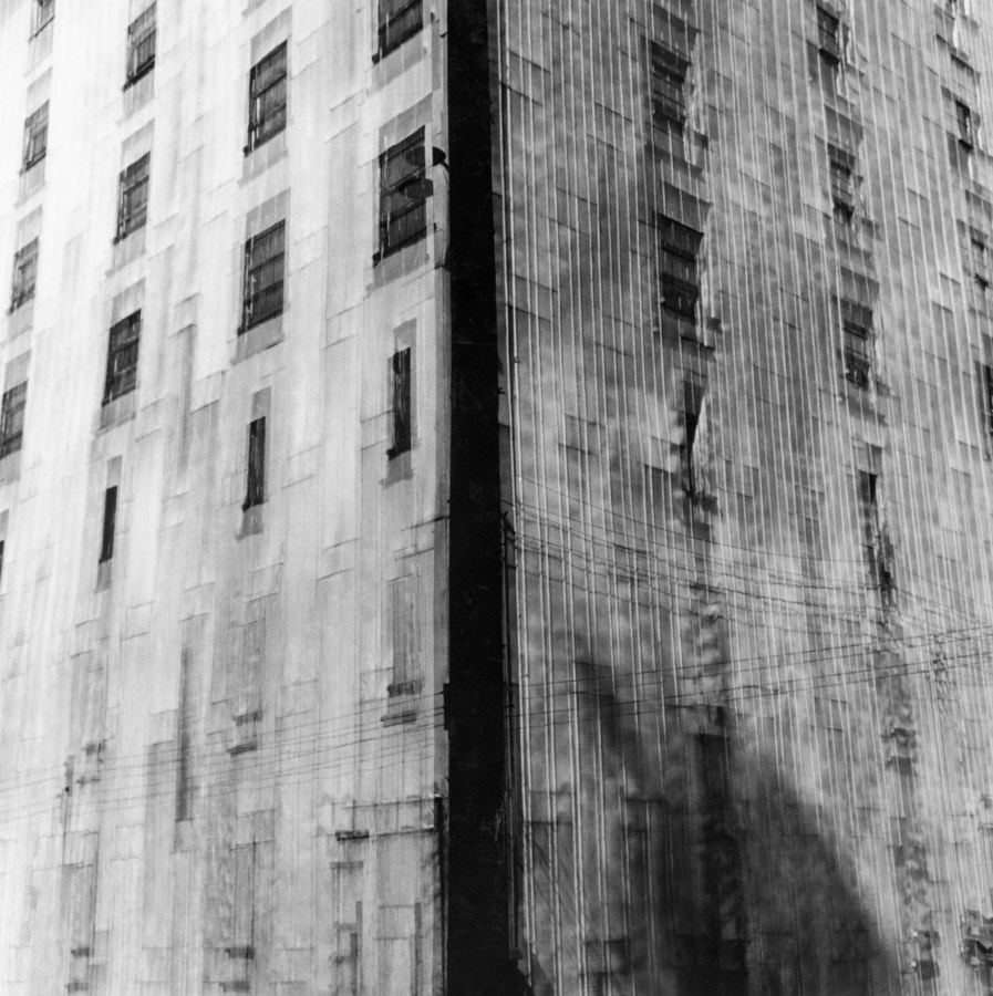 Black-and-white multiple-exposure photograph of the corner of a tall city building with evenly spaced rectangular windows