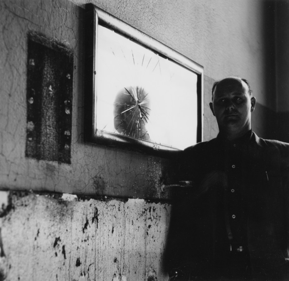 Black-and-white photograph of a man standing next to a cracked mirror