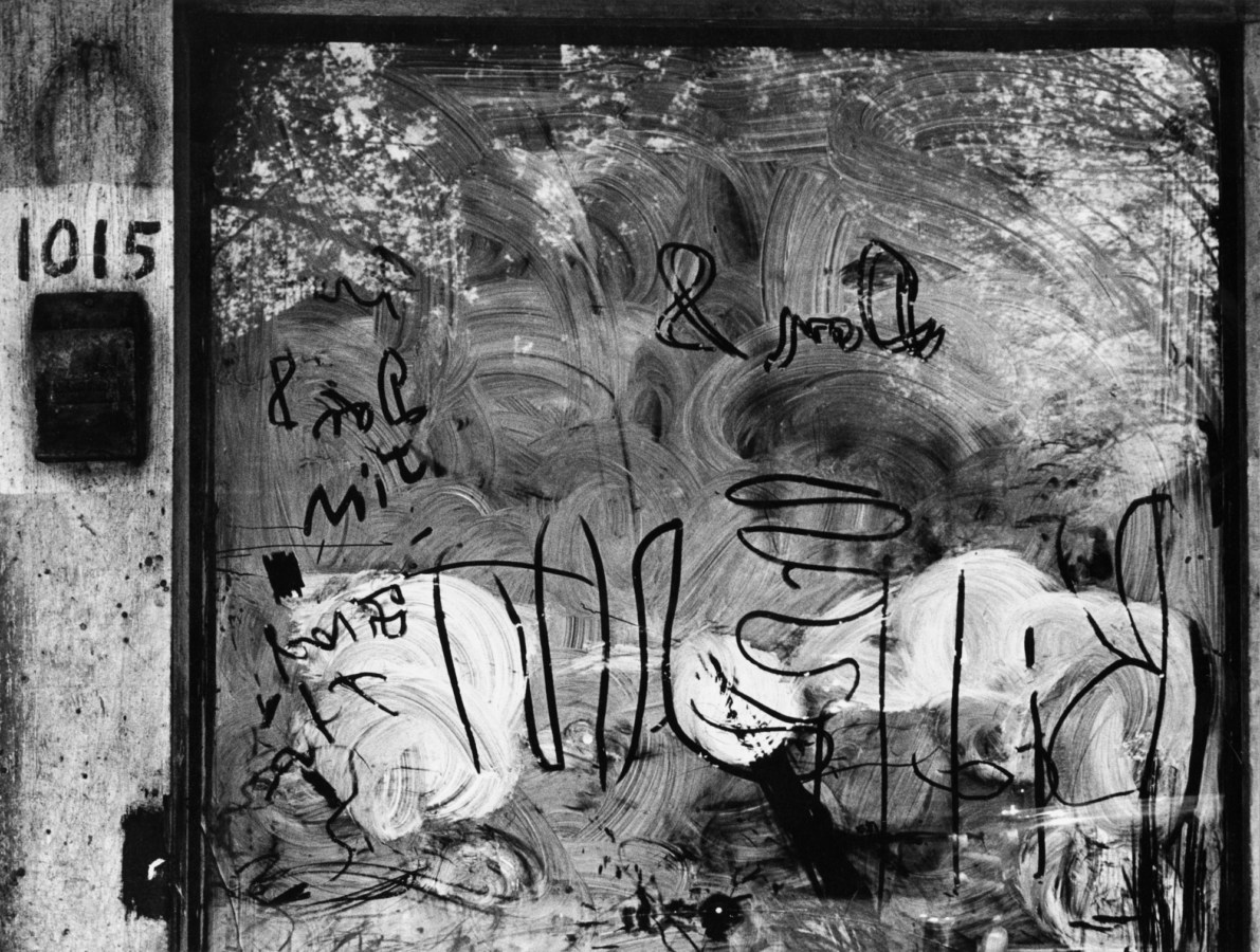 Black-and-white photograph of a soaped-up window with squiggles and letters drawn into it