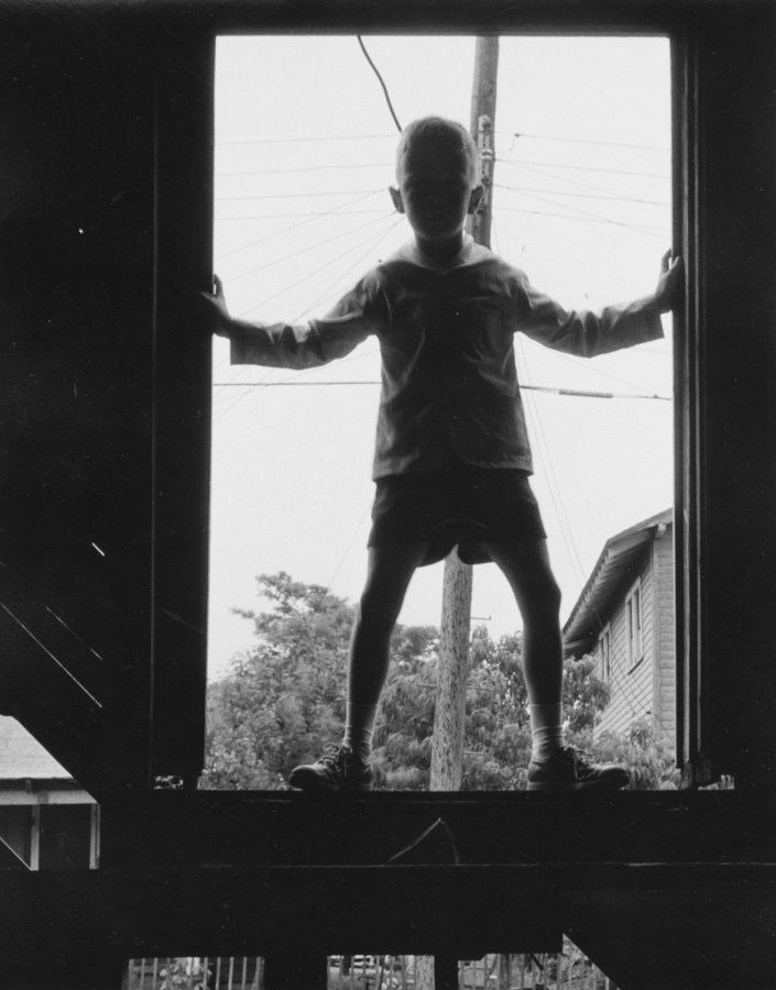 Black-and-white photograph of a young boy standing in a window frame