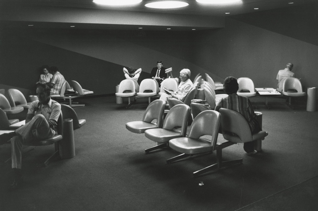 Black-and-white photograph of a waiting area with passengers scattered among seats