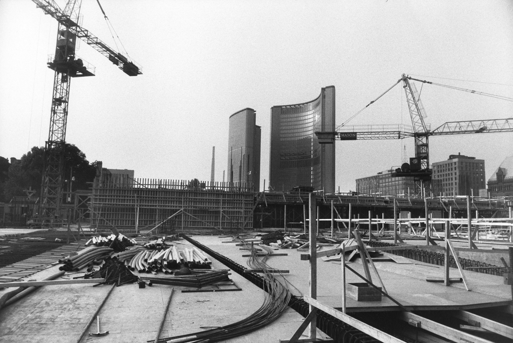 Black-and-white photograph of two cranes overlooking an empty construction site