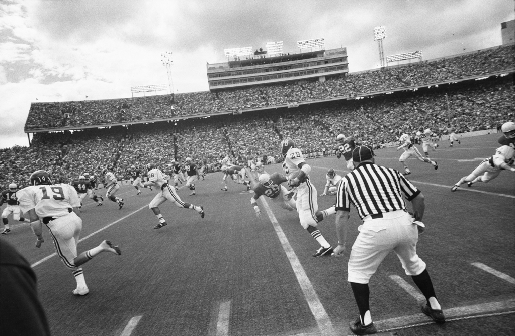 Black-and-white photograph of an American football game in progress against the backdrop of a full stadium