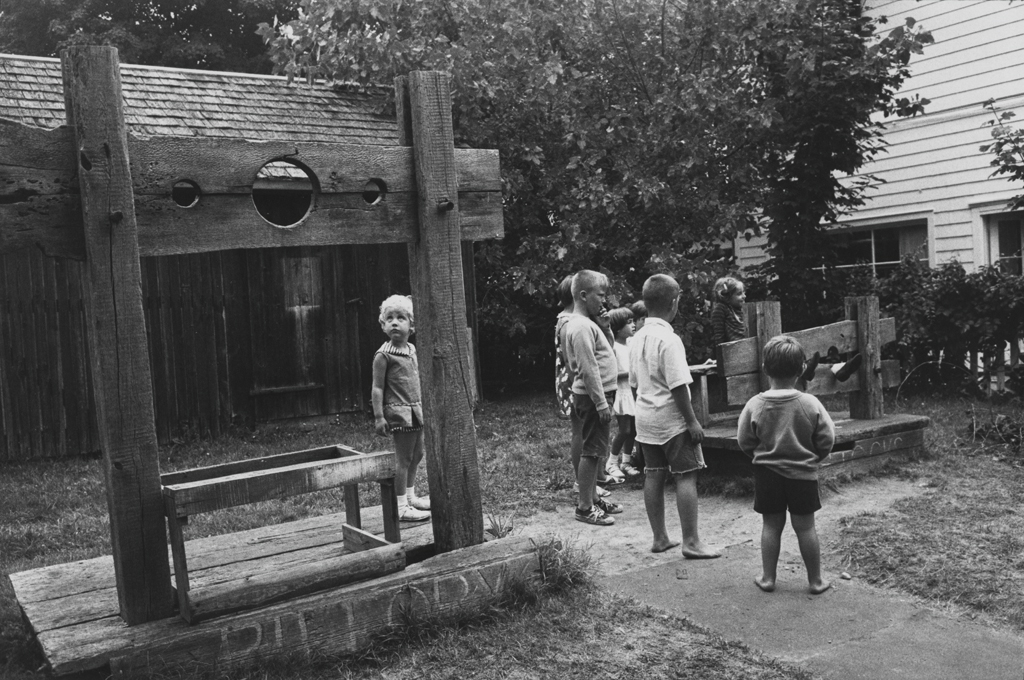 Black-and-white photograph of a group of children inspecting empty wooden stocks