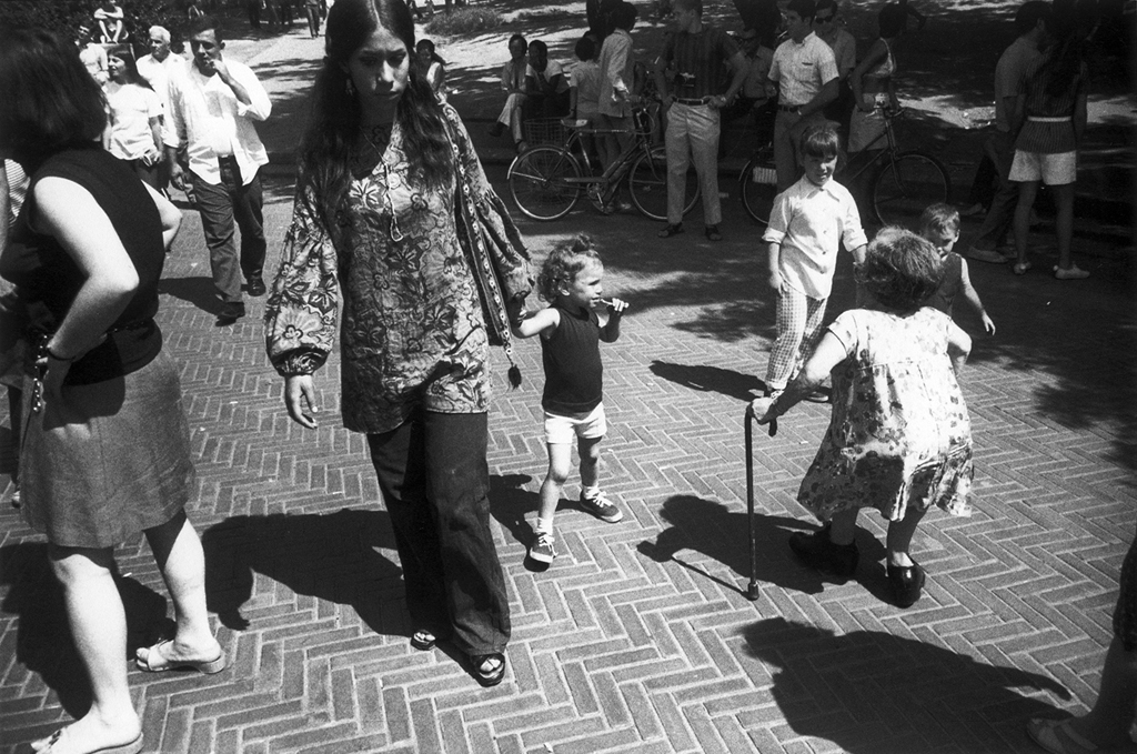 Black-and-white photograph of a woman walking down a brick pavement holding a young girl's hand