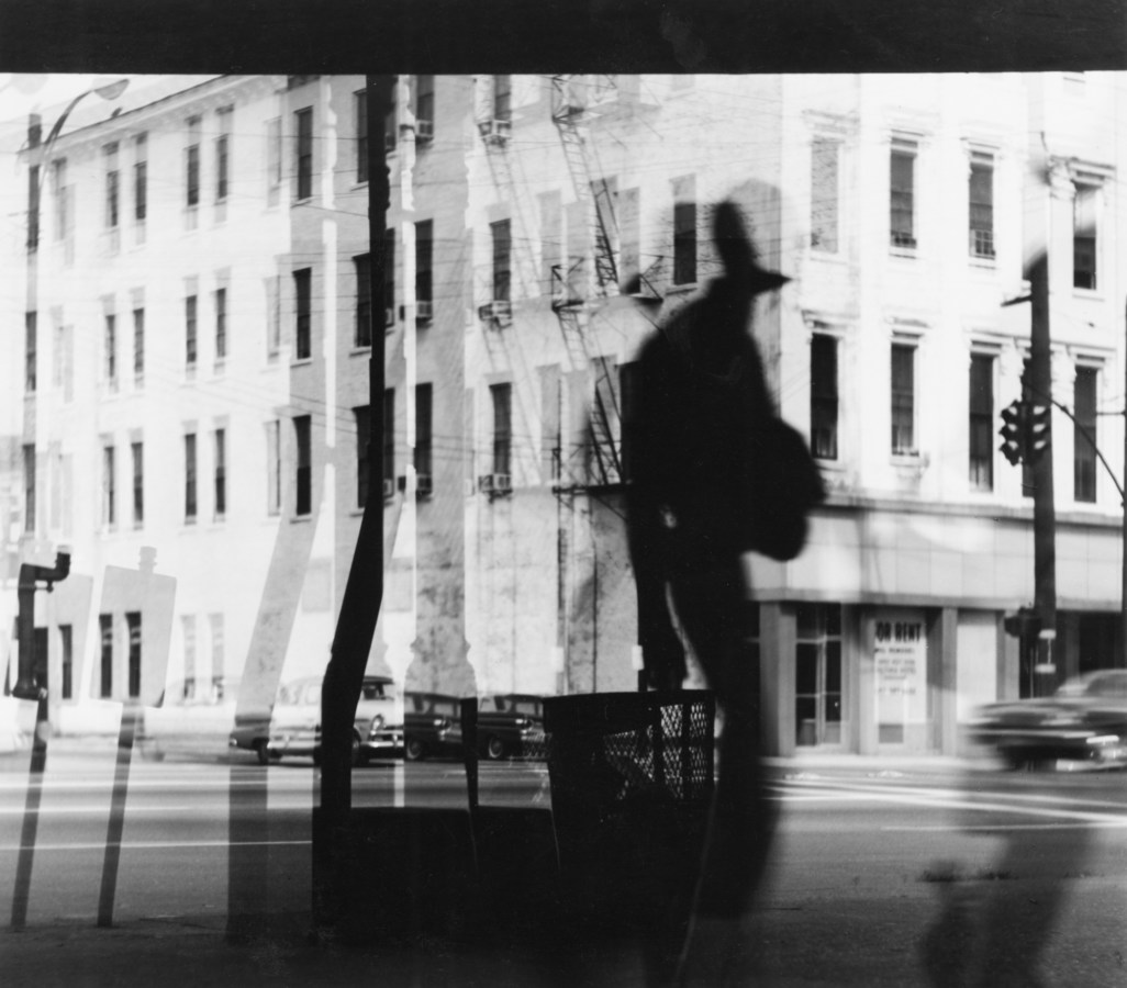 Black-and-white multiple-exposure photograph of a person's reflection against a city street
