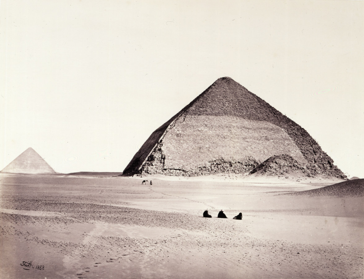 Black and white photograph of two pyramids with three people sitting in the foreground