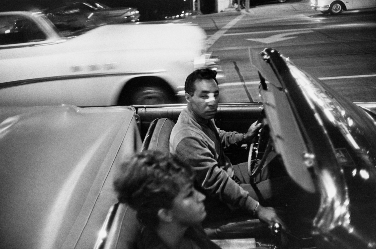 Black-and-white photograph of a man and woman in a moving convertible car
