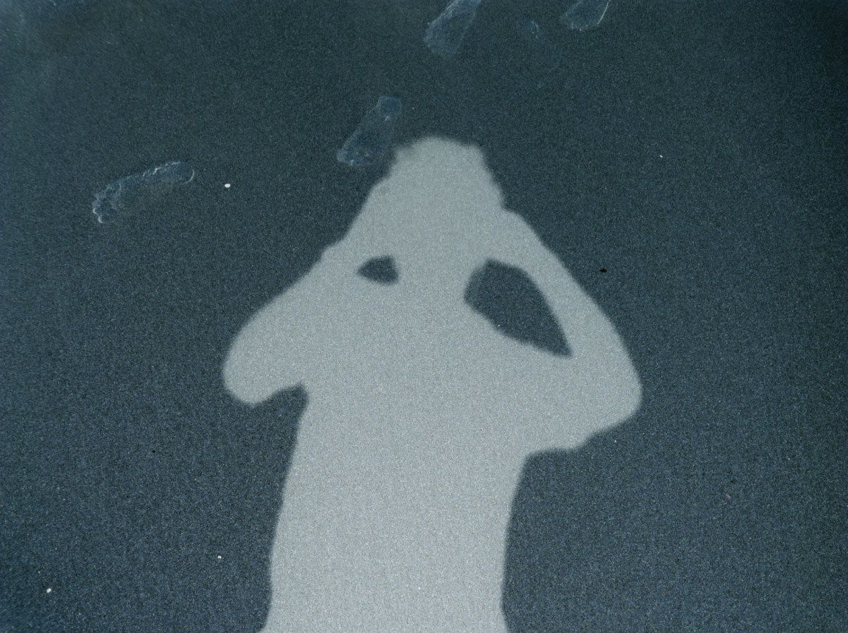 Inverted color photograph of the shadow of the photographer taking a photo of footprints in the sand