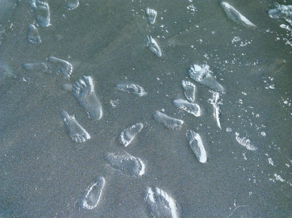 Inverted color photograph of shallow footprints in sand