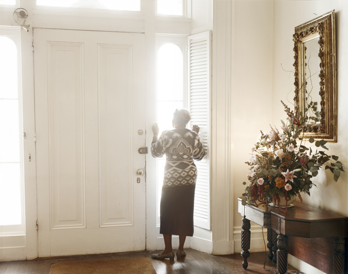 Color photograph of a woman peering through a light-filled window in a foyer