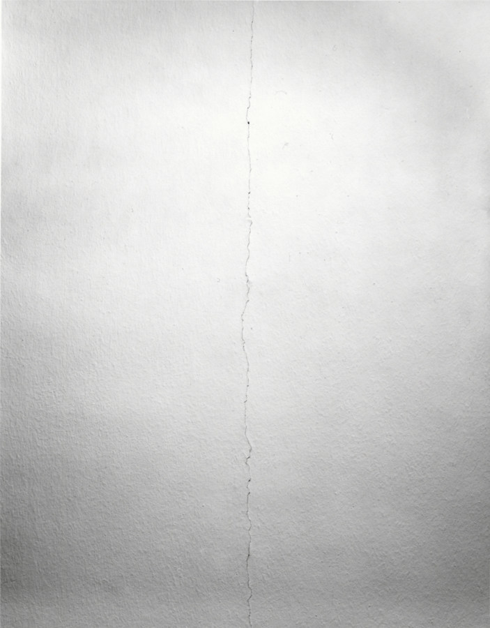 Black and white photograph of a long straight crack in a white wall