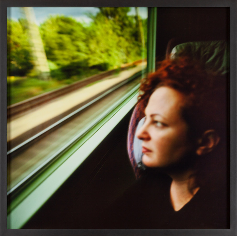Color portrait of woman looking out through the window of a moving train, blurred tracks visible outside