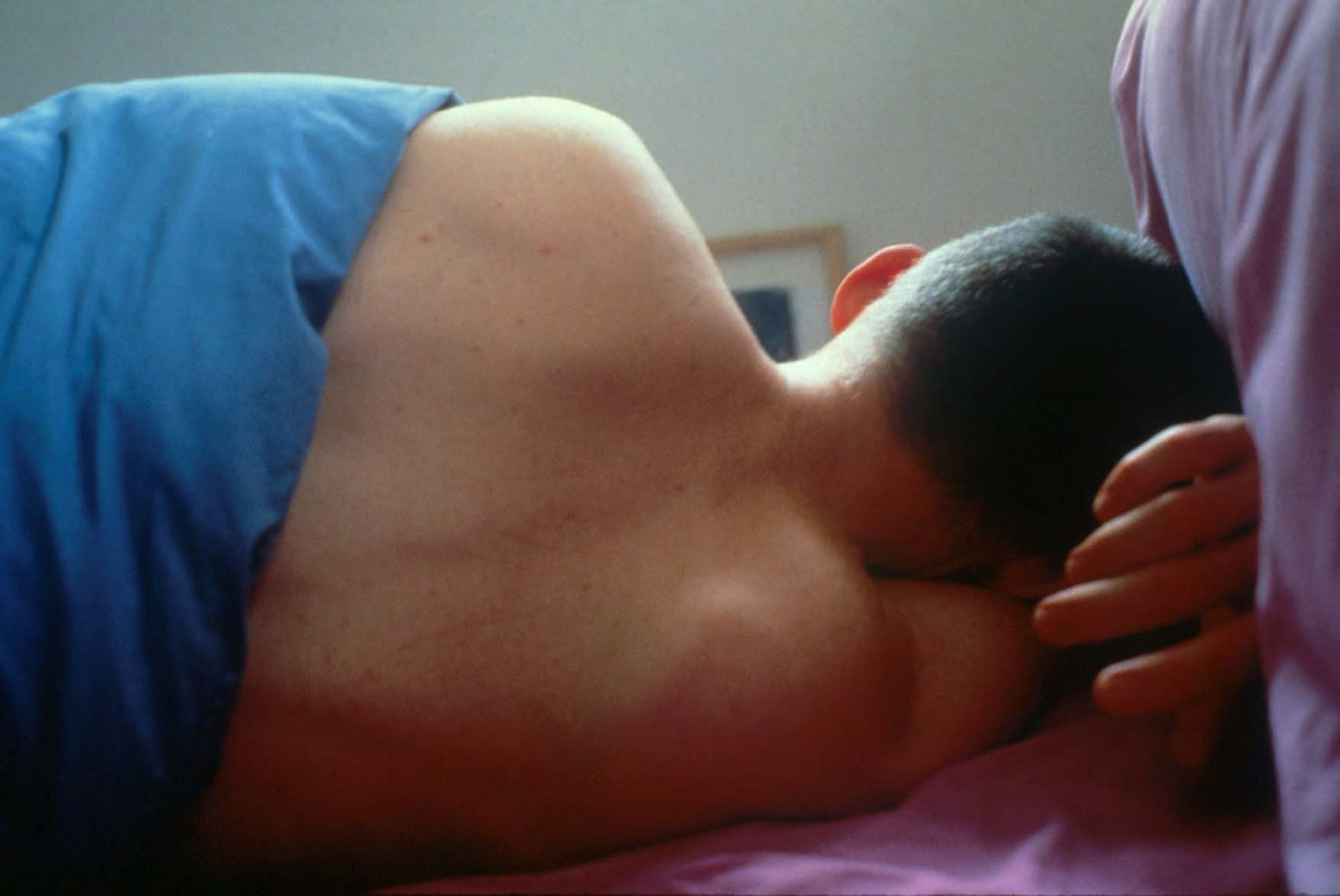 Color photograph of a person in bed with their back to the viewer