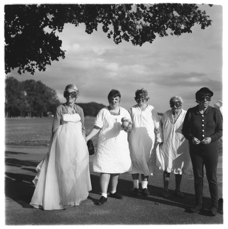 Black and white photograph of five masked people standing in front of a wide lawn