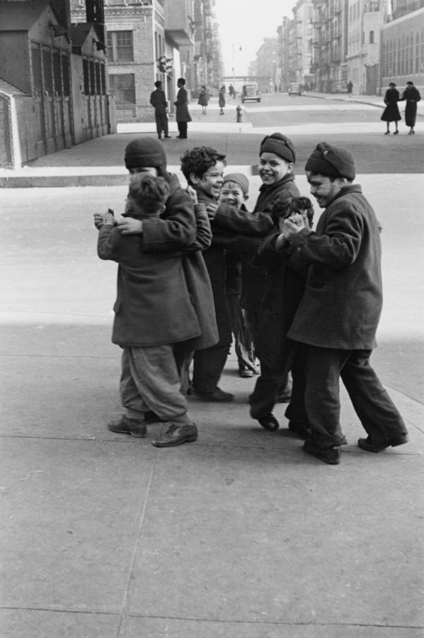 Black and white photograph of a group of children in oversized coats walking down a city sidewalk