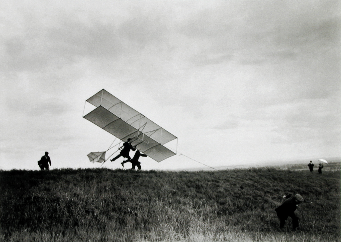 Black and white photograph of people launching an early airplane by hand in an open field