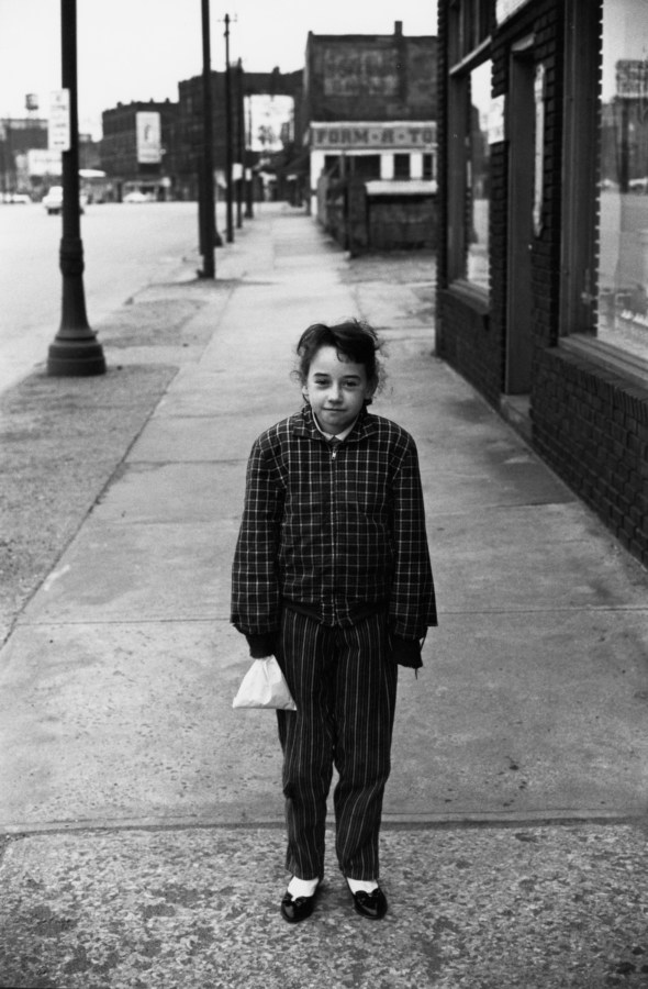 Black and white photograph of a young girl standing on an empty sidewalk