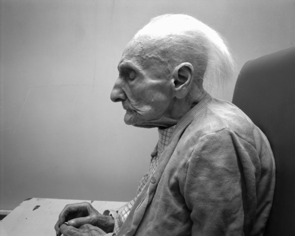Black and white photograph of the profile of an elderly person seated with their eyes closed