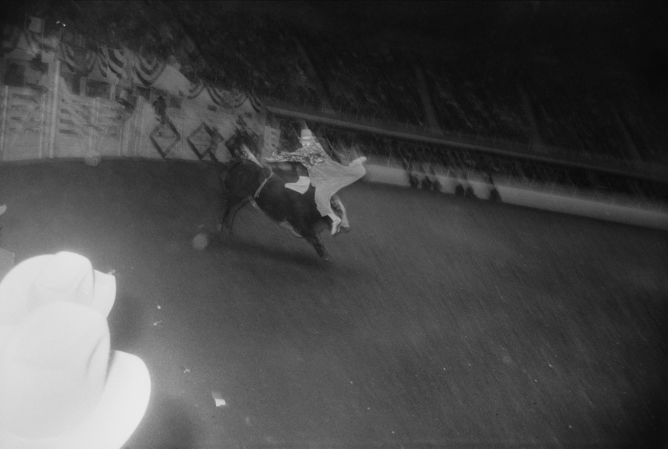 Black-and-white photograph of a man dressed as a clown being thrown from the back of a bucking bull