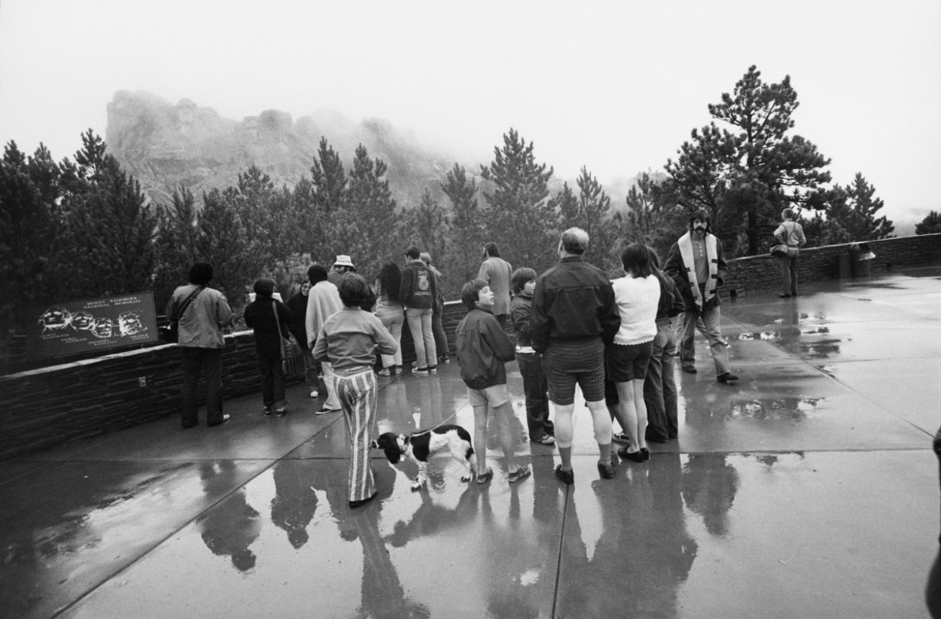 Black-and-white photograph of a family of tourists approaching a look out point of an overcast rock outcrop