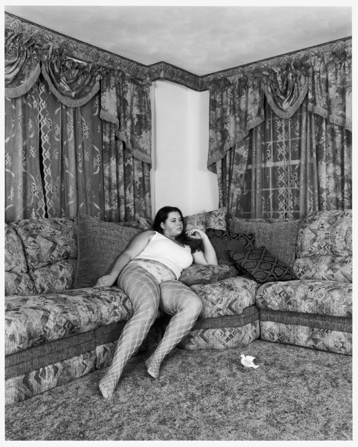 Black-and-white photograph of a woman reclining on an overstuffed corner sofa