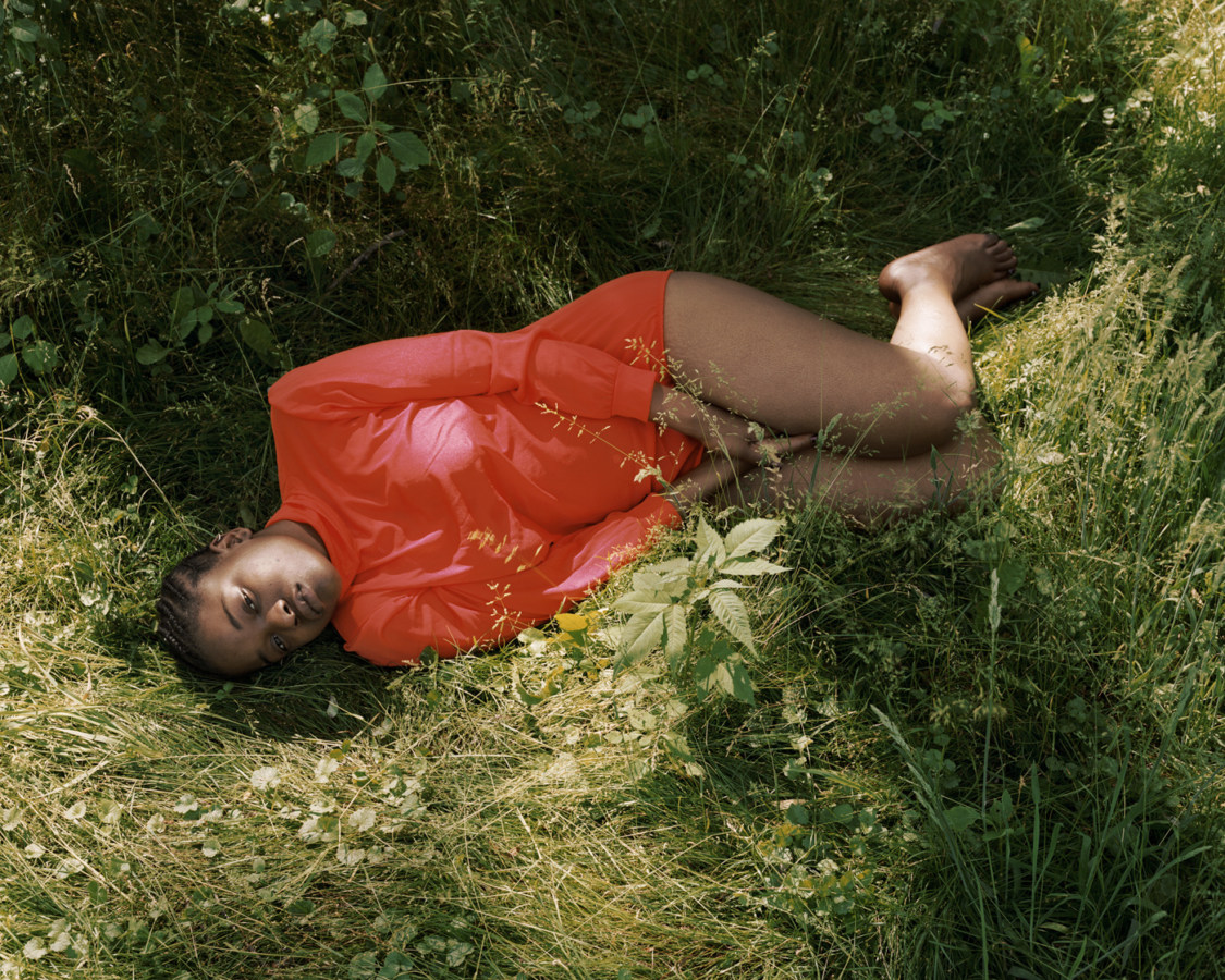 Color photograph of a woman in a red shirt lying on her side in long grass