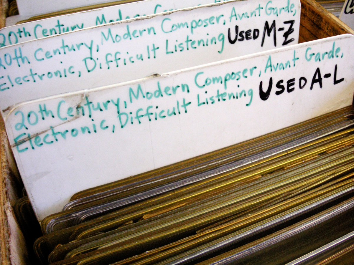 A color photograph of dividers in a bin at a record store, labeled with the genres of the records.