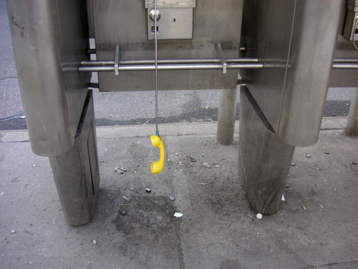 A color photograph of a pay phone, with the yellow phone dangling off the receiver.