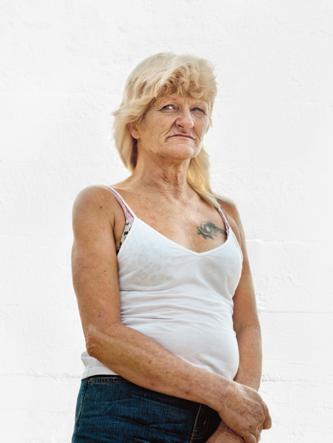 Color photographic portrait of a middle-aged woman in a white tank top standing in front of a blank white wall