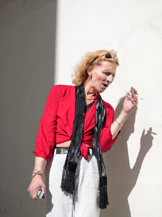 Color photograph of a woman in a tied red top and black scarf holding a cigarette