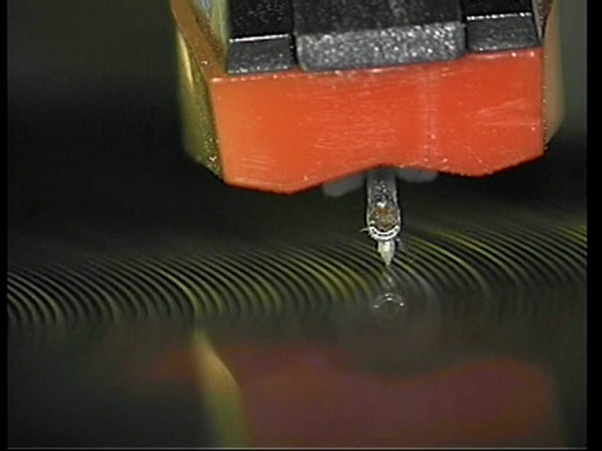 Color video still of a record player's needle hovering above a vinyl record