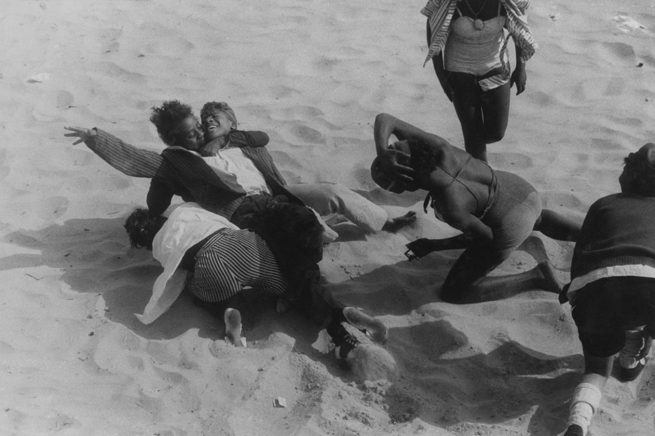 Black-and-white photograph of six people embracing and kneeling on the sand