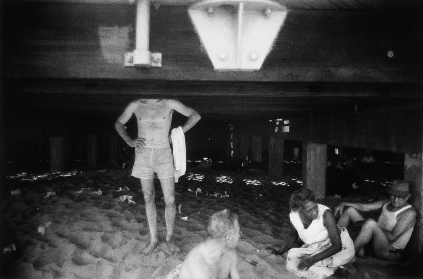 Black-and-white photograph of people in bathing suits beneath a boardwalk