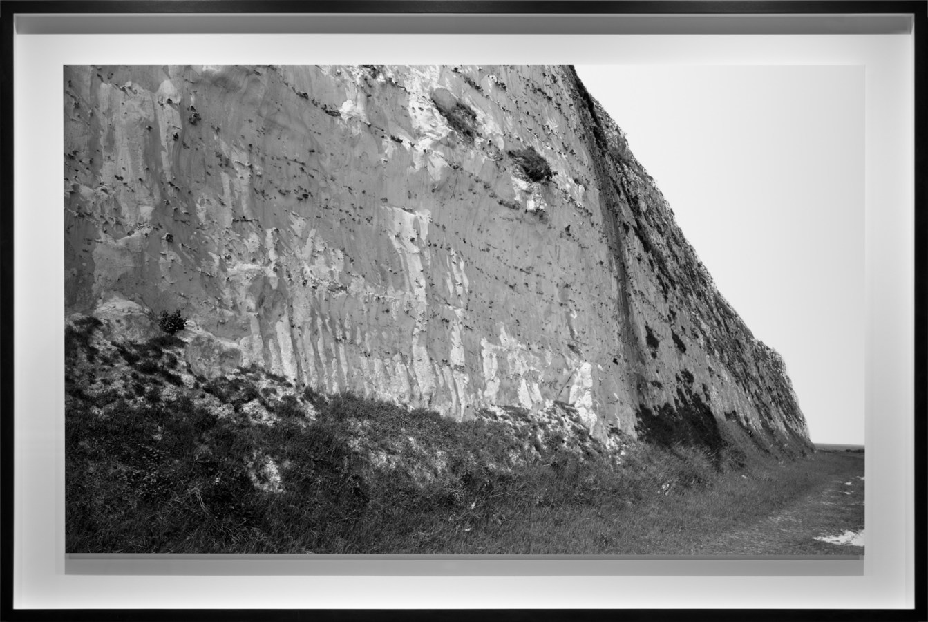 Black-and-white photograph of the base of a bare pale cliff face