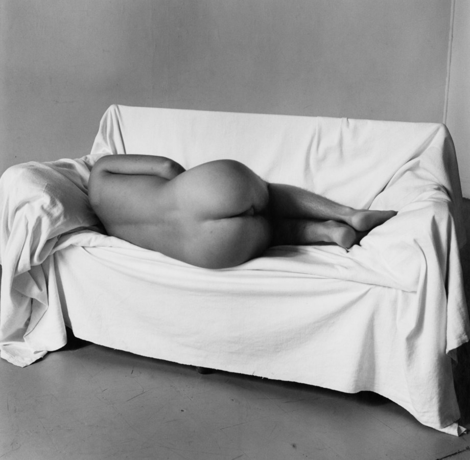 Black and white photograph of a nude man laying down in fetal position