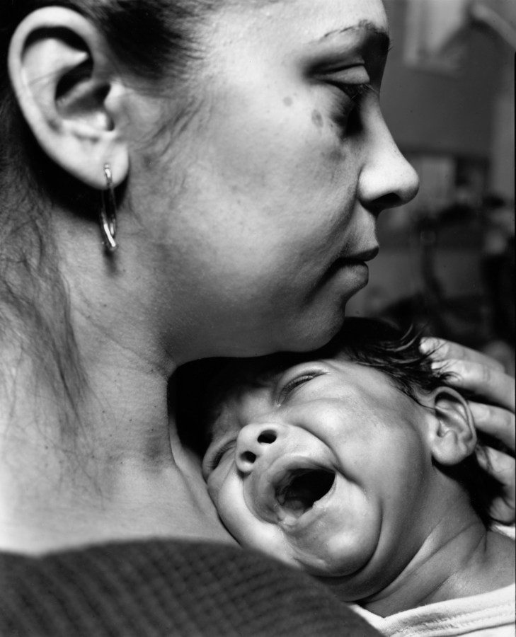 Black-and-white photograph of a woman cradling a crying baby's head beneath her chin