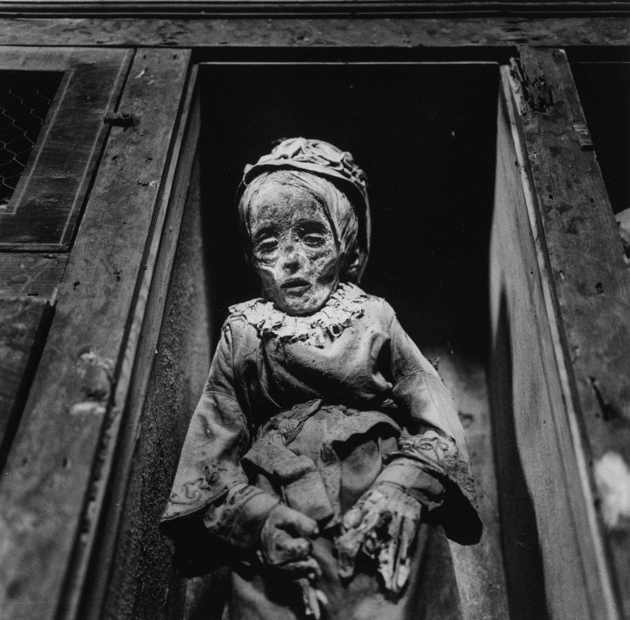 Black-and-white photograph of a preserved child's body propped up in a wooden alcove