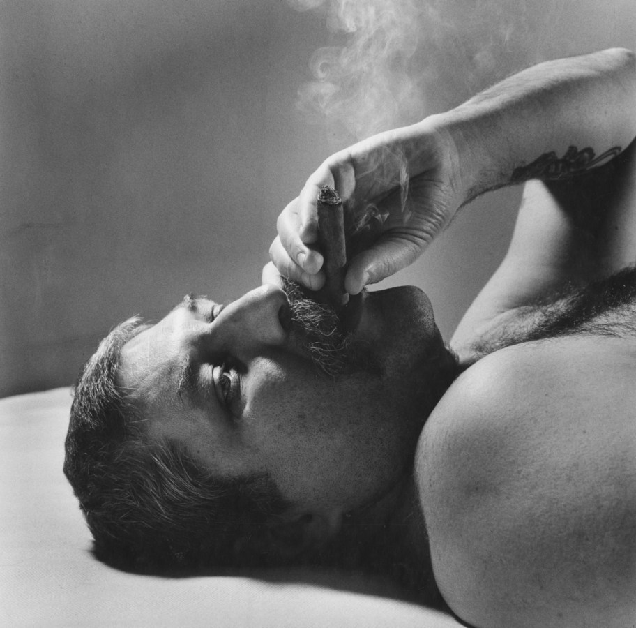 Black and white photograph of a man smoking a cigar while lying down