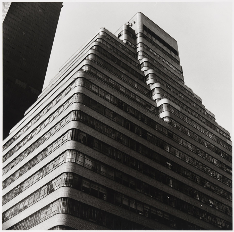 Black and white photograph from below of a stepped building with rounded corners