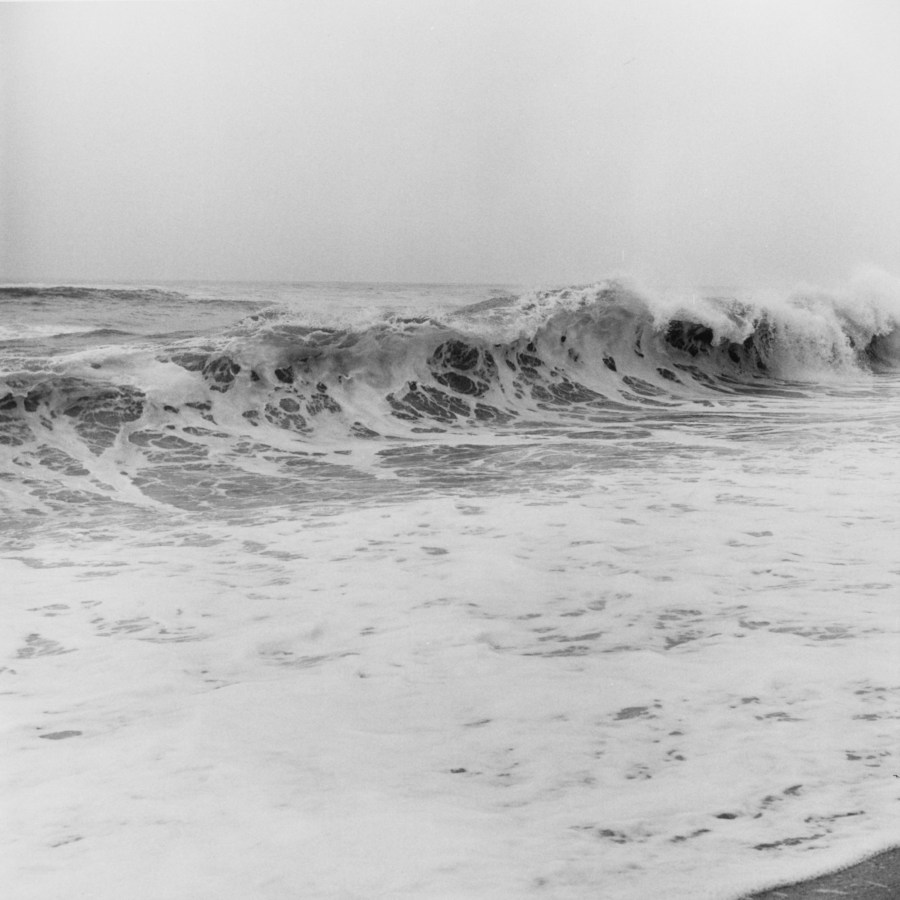 Black-and-white photograph of white water and a wave crashing on the seashore