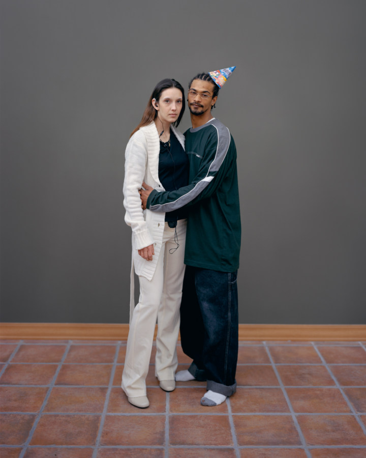 Color photograph of a standing couple against a bare gray wall