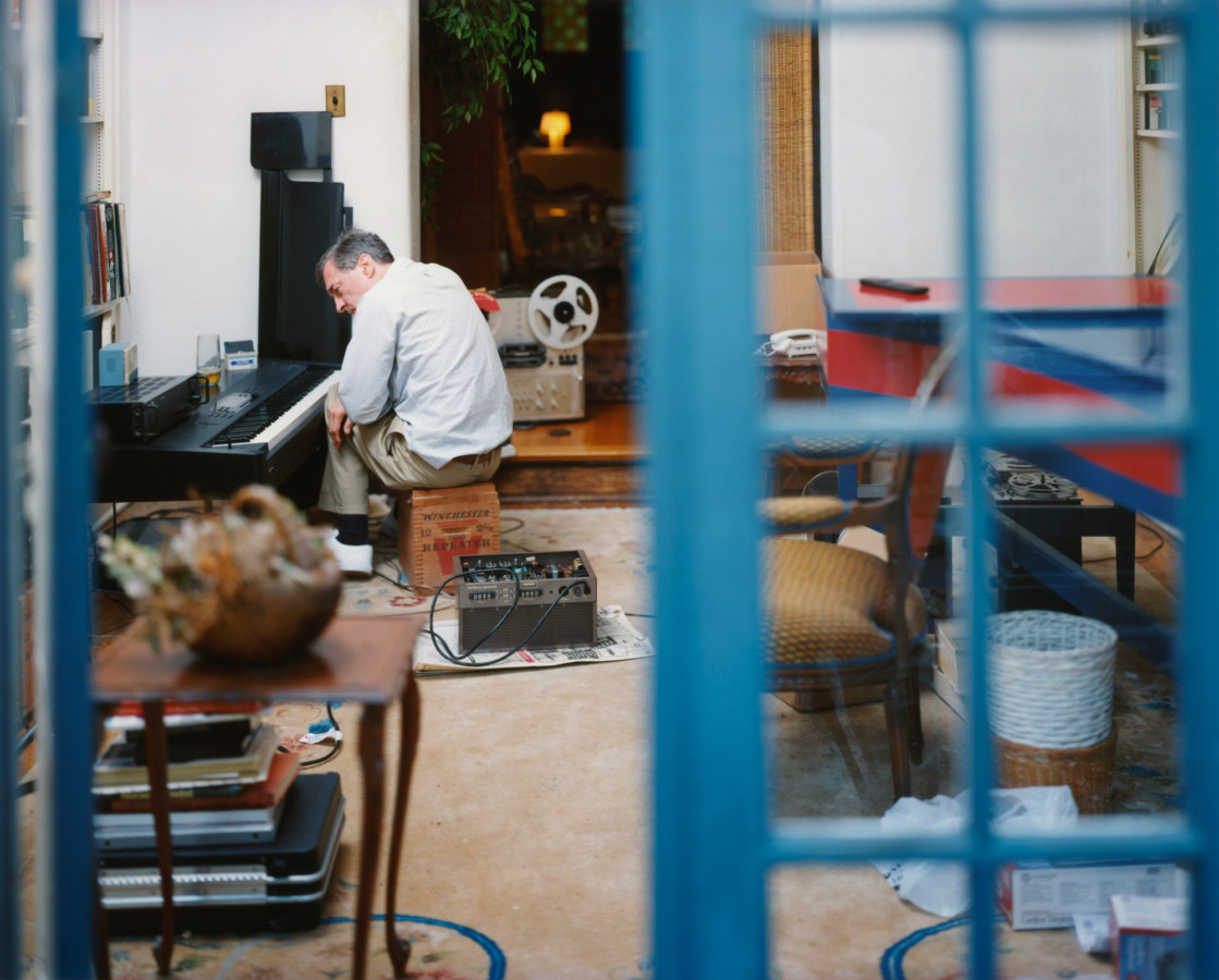 Color photograph of a man seated at a piano keyboard through an open blue French door