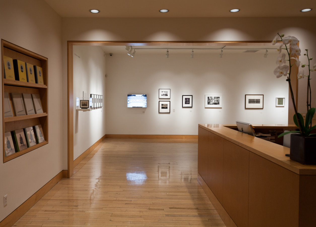 Color image of gallery entryway leading to an exhibition of framed photographs on a white wall