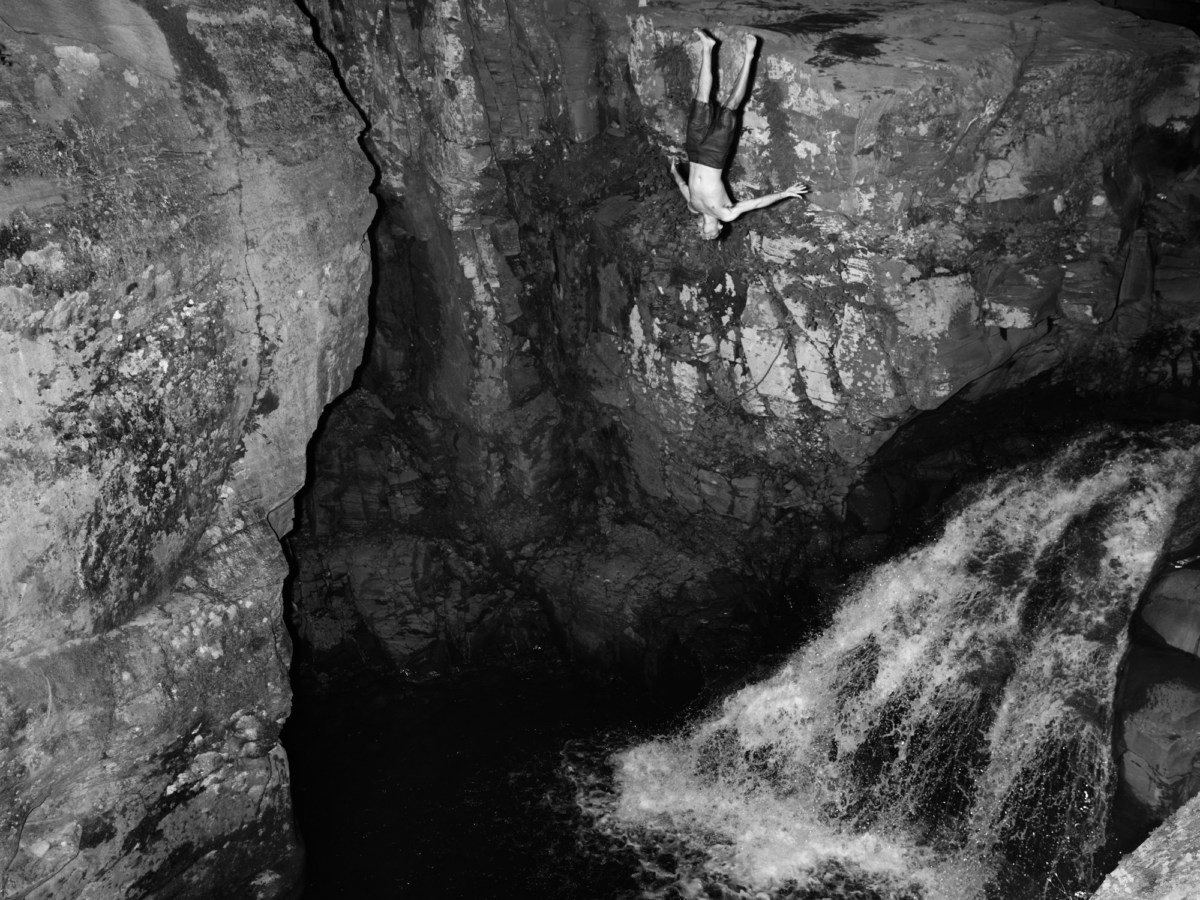 Black and white photograph of a person jumping off a cliff into water