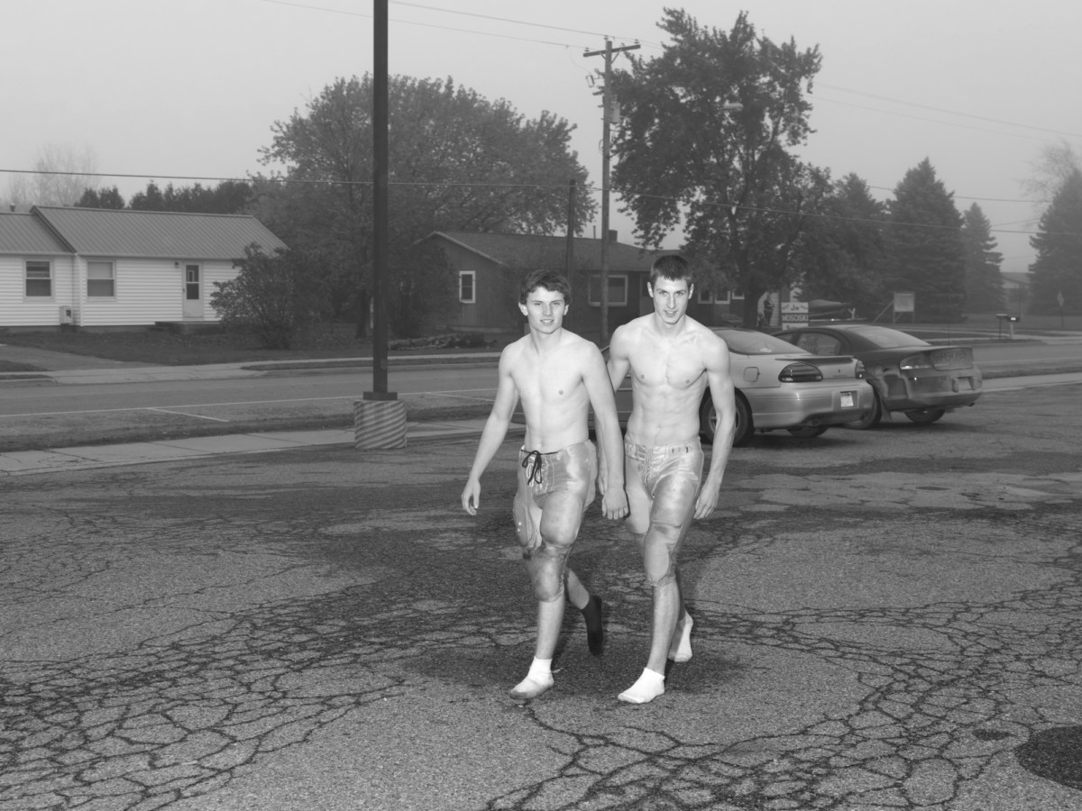 Black and white photograph of two shirtless football players walking in parking lot