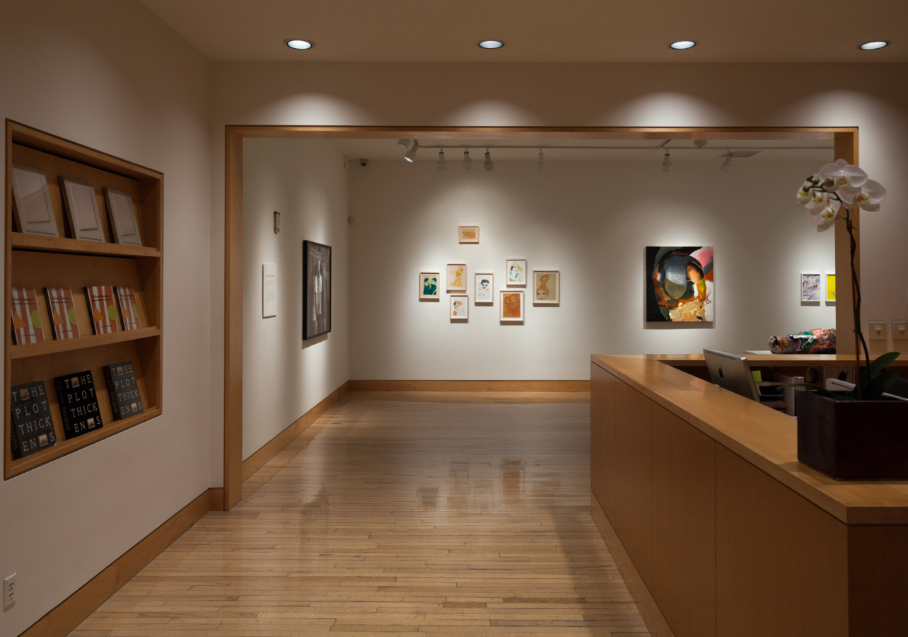 Color image of a gallery entryway exhibiting framed works and sculptures