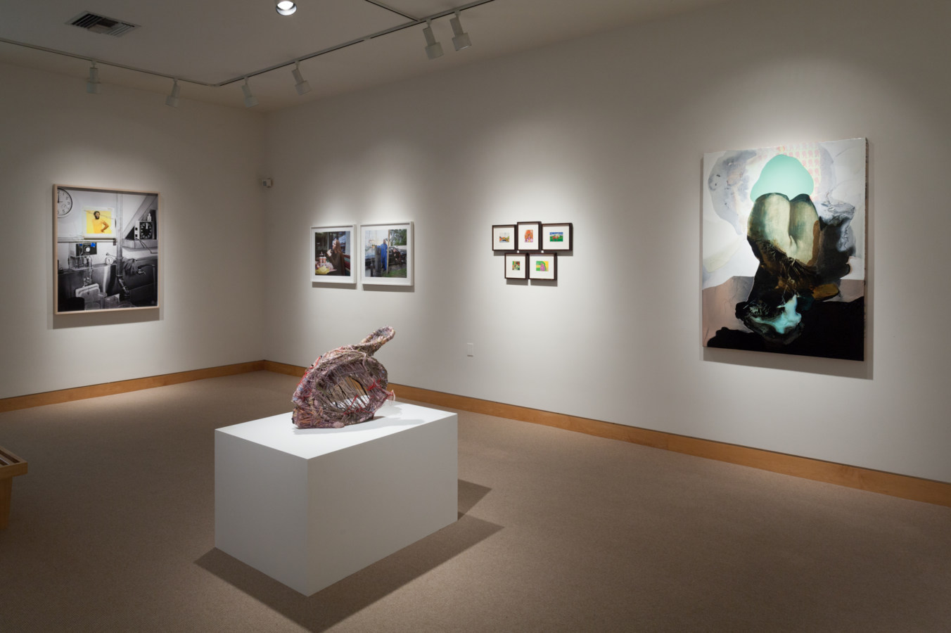 Color image of exhibition depicting artworks both framed and sculptural within gallery
