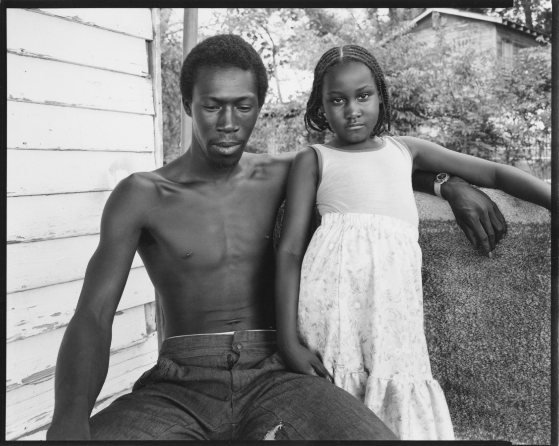 Black and white photograph of a shirtless man with young girl who looks directly at viewer