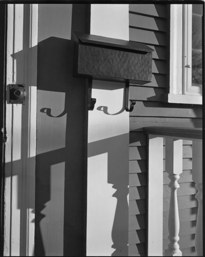 Black and white photograph of a mailbox on a front porch
